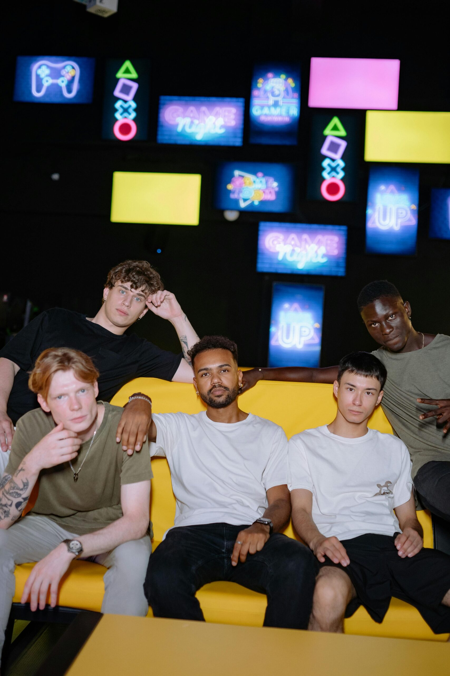 Group of diverse male gamers sitting on a couch indoors, enjoying game night with vibrant screens.